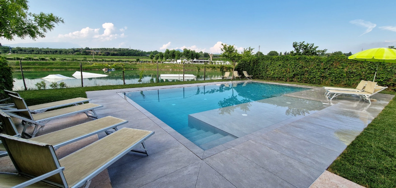 Piscina all'aperto con vista sul lago e prato.