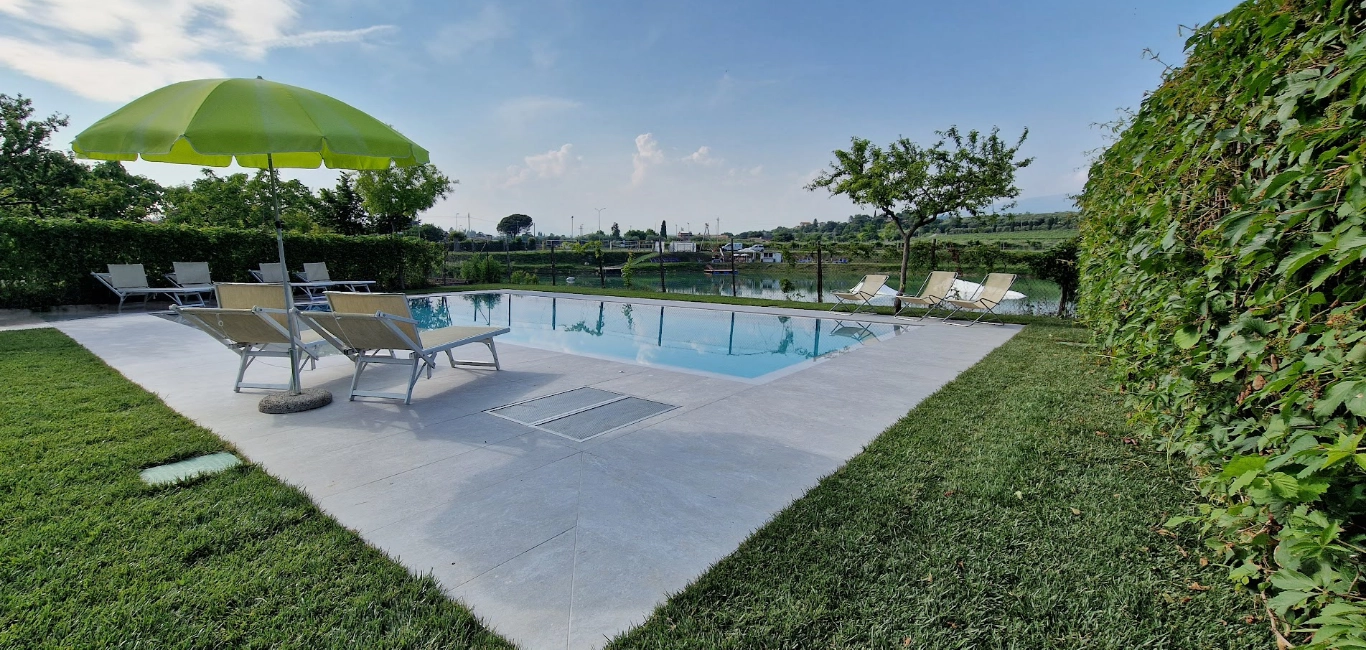 Piscina all'aperto con lettini e ombrellone verde.