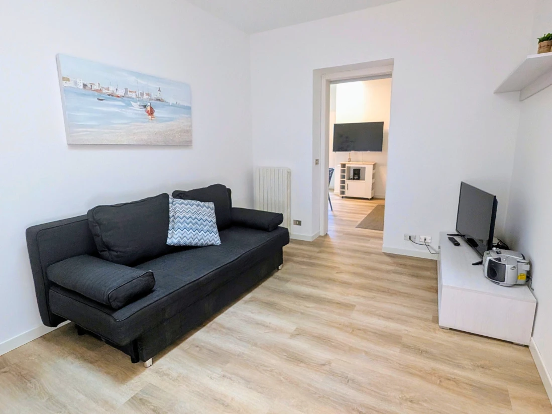 Soggiorno con divano nero e TV a muro.